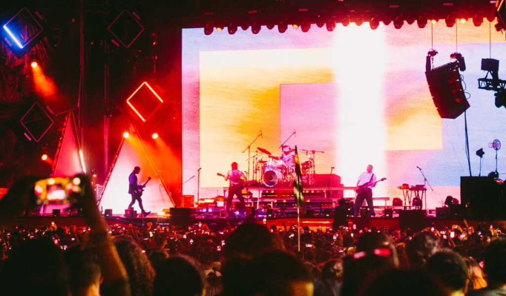 A view from a distance of a band on stage with bright colorful screens behind them