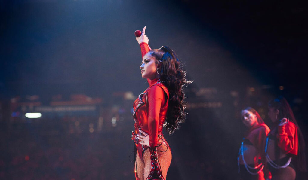 Becky G in a red costume holding her hand up to the crowd