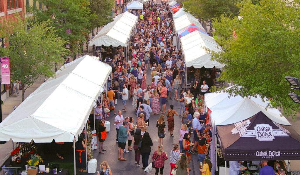 A bustling crowd moving between two rows of tent canopies at a food festival
