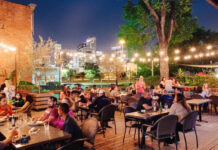 Where to Happy Hour in EaDo An evening view of the outdoor patio at Around the Corner with strings of lights and Downtown skyscrapers