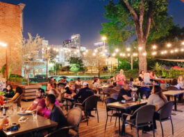 An evening view of the outdoor patio at Around the Corner with strings of lights and Downtown skyscrapers