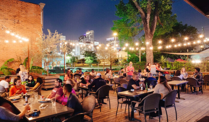 An evening view of the outdoor patio at Around the Corner with strings of lights and Downtown skyscrapers