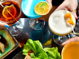 Four colorful drinks viewed from above with appetizers