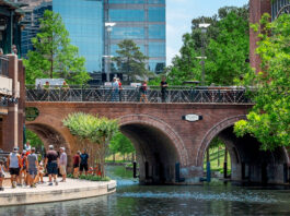 A sunny scene of crowds walking along a river and over a bridge