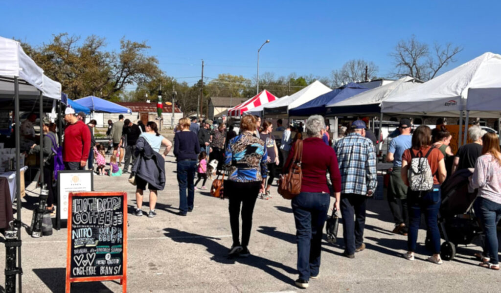 People walking through two rows of stalls at a farmers market