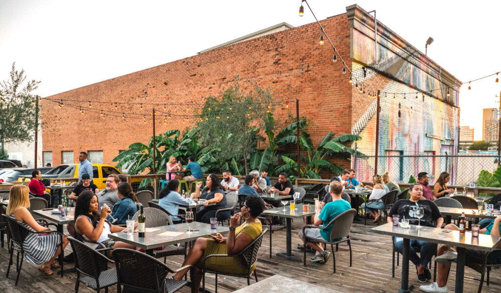 An outdoor patio with tables of patrons sat next to a large brick building