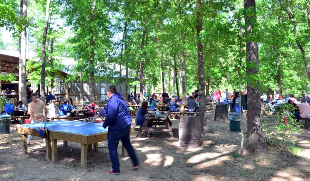 People playing ping pong and gathered around picnic tables at an outdoor brewery