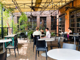 A covered patio with leafy green plants and people dining