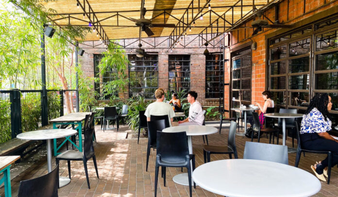 A covered patio with leafy green plants and people dining