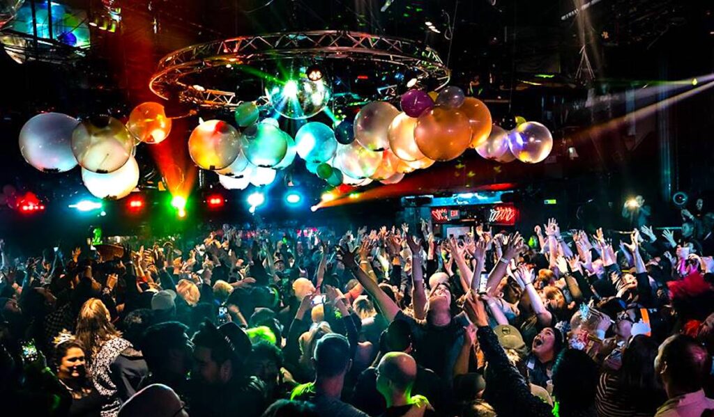 A crowded dance floor at a nightclub with balloons and a disco ball overhead