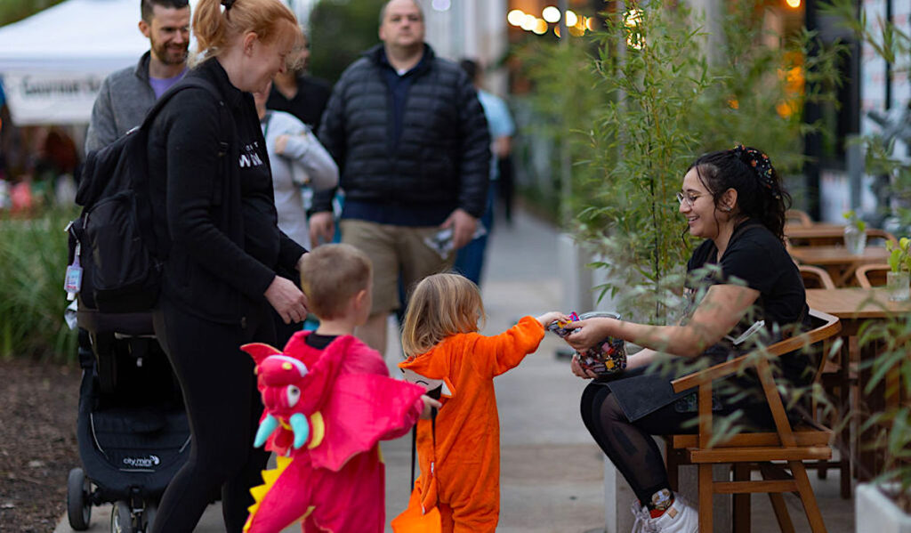 Two children in costumes take candy from a person