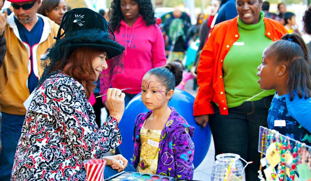 A face painter putting purple paint lines on a child's face