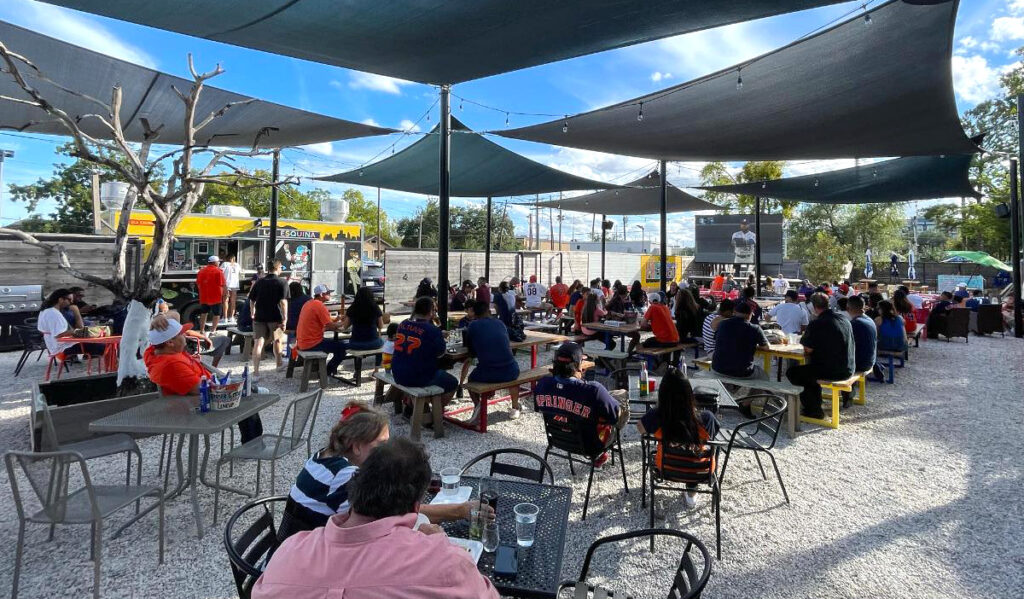 An outdoor patio with mesh covering, filled with people watching sports