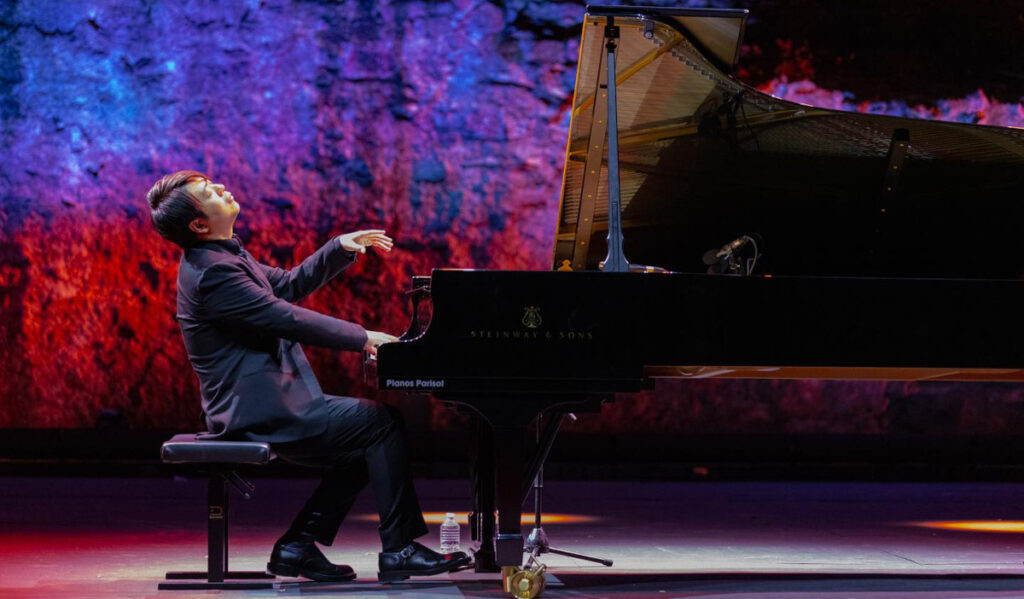 Pianist Lang Lang performs on stage with red and blue lights behind