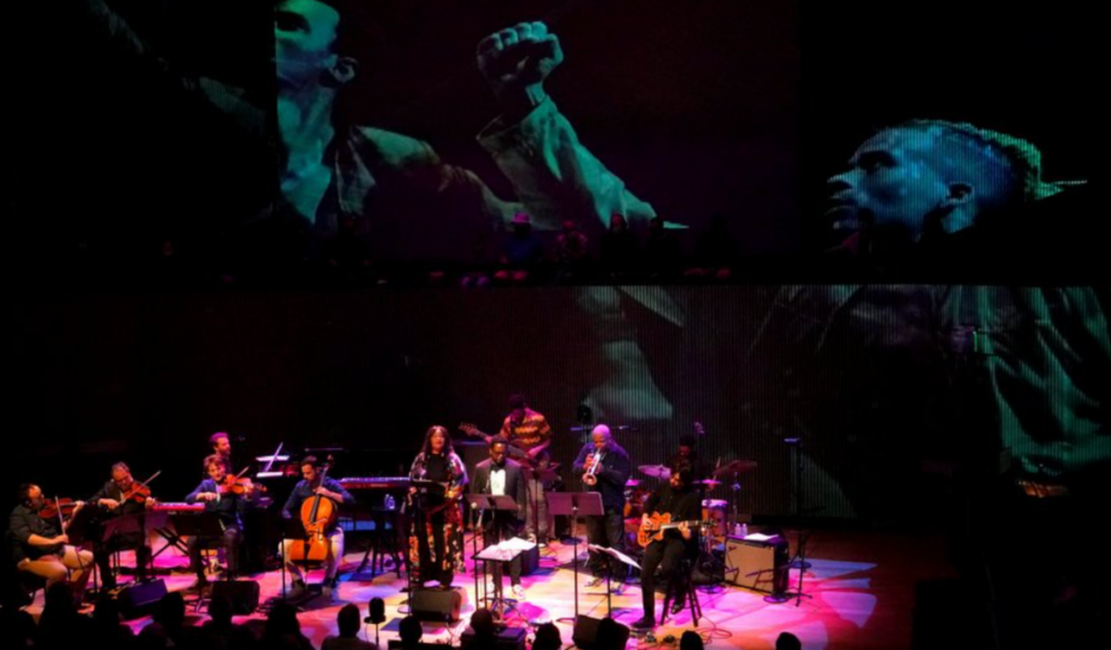 An orchestra performs while large images of people raising fists are projected behind them
