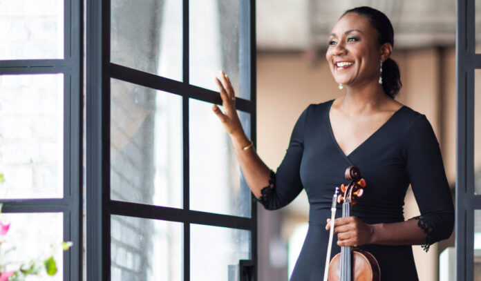 Rachel Jordan poses near a glass window while holding a violin