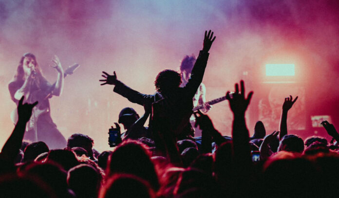 A fan in silhouette crowd surfs at a concert while the band plays on stage