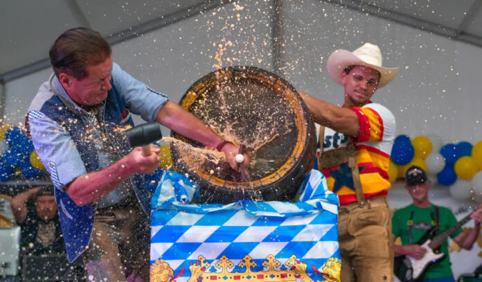 Two people tap a wooden keg and beer spurts in all directions