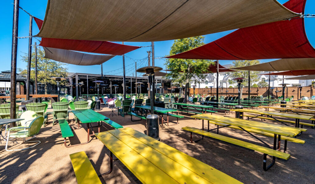 An outdoor patio with picnic tables and seating under mesh canopies