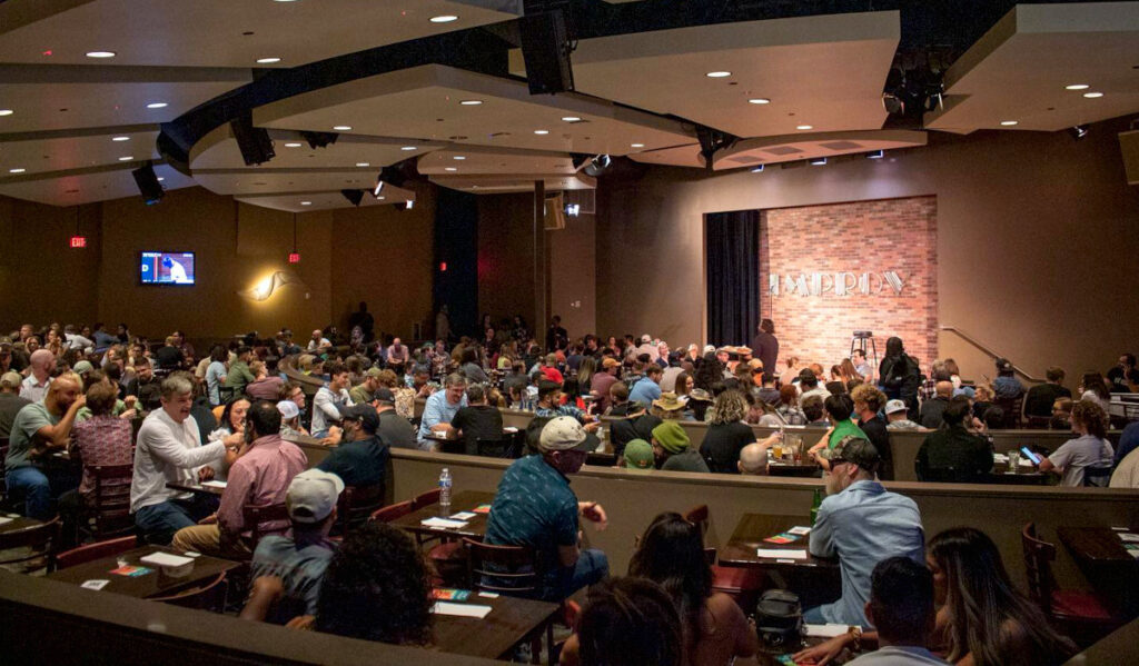 Interior of Houston Improv with people sitting at tables and an empty comedy stage