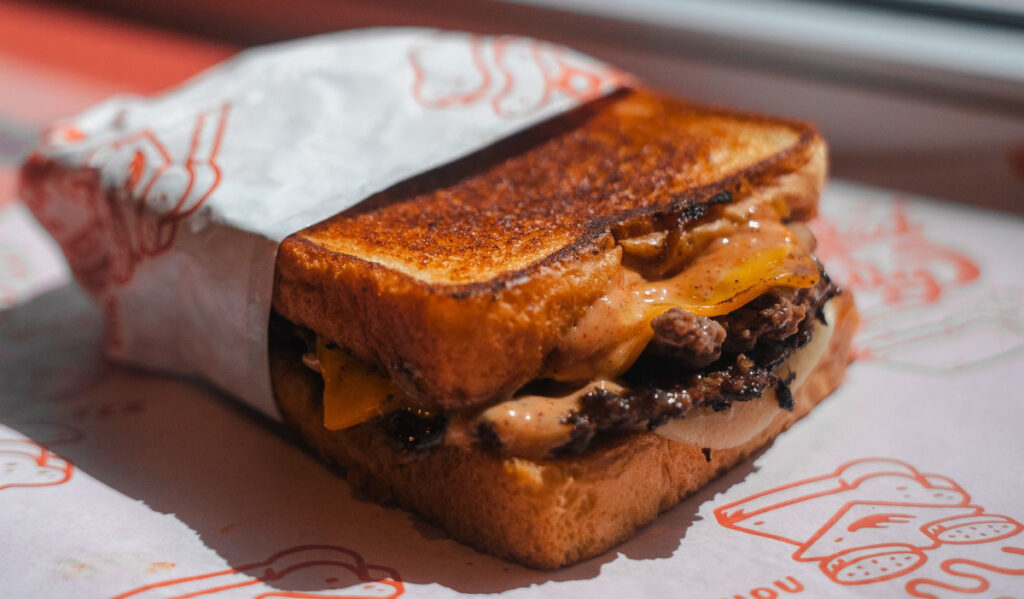 A close-up of a patty melt sandwich on toasted bread in a paper wrap