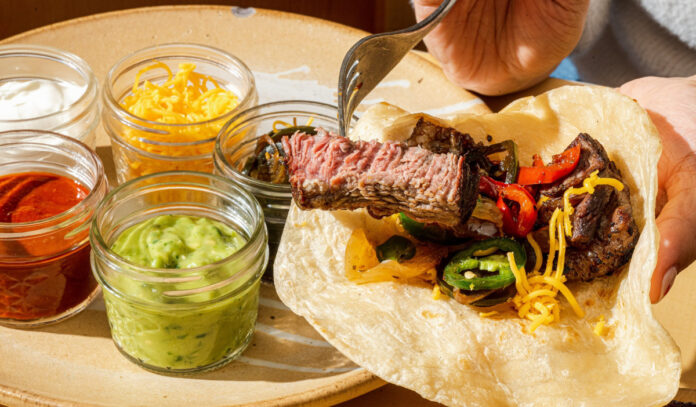 A hand filling a tortilla with steak fajita