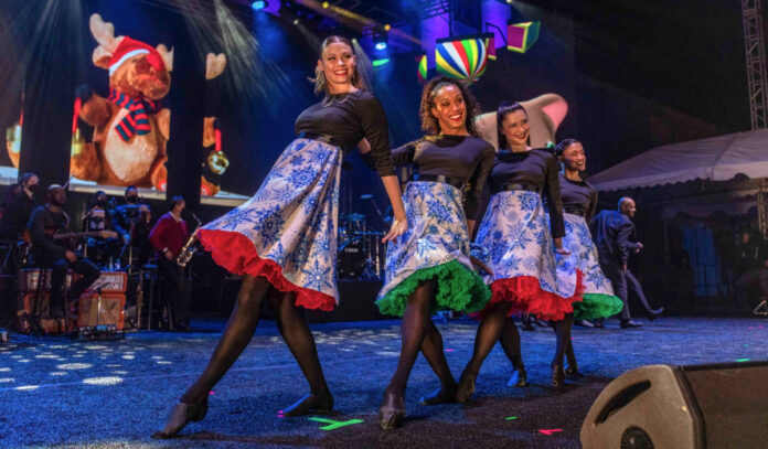 Four women in festive dresses dancing in sync on a stage