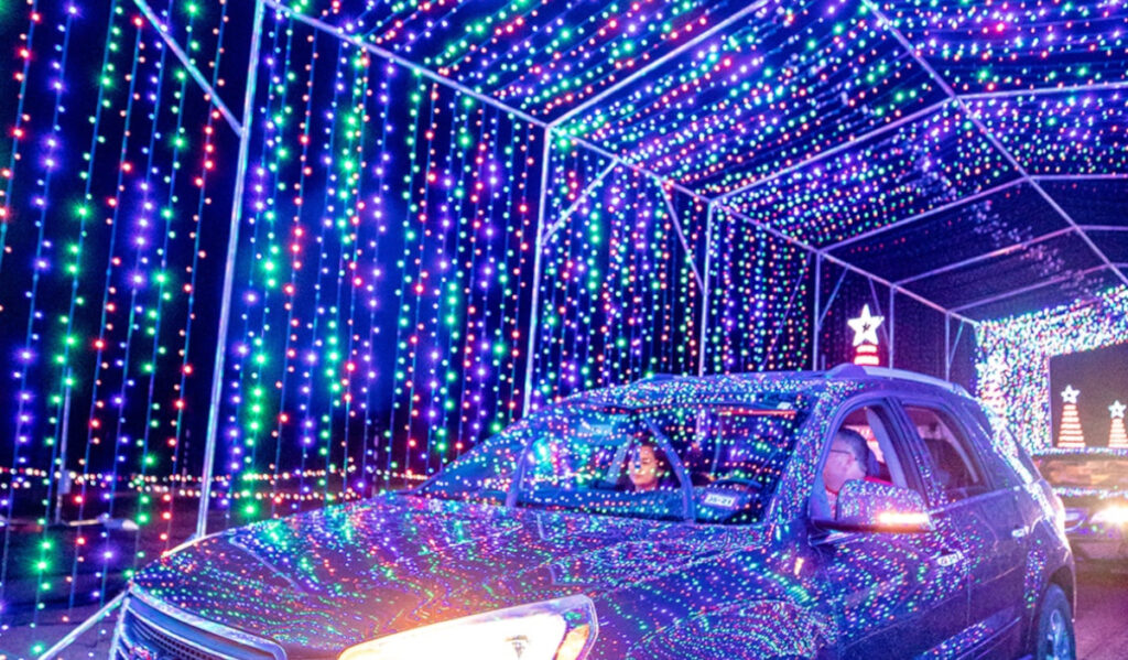 A car drives through a tunnel of Christmas lights that reflect off the car