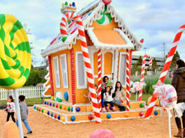 A family sits on the steps of a large gingerbread house for a photo