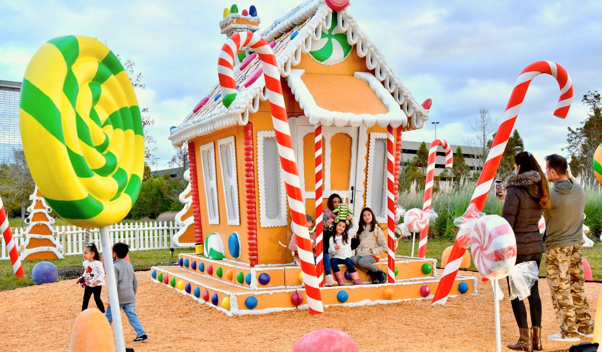 A family sits on the steps of a large gingerbread house for a photo