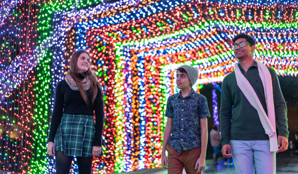 Three people walking through a multicolored tunnel of LED lights