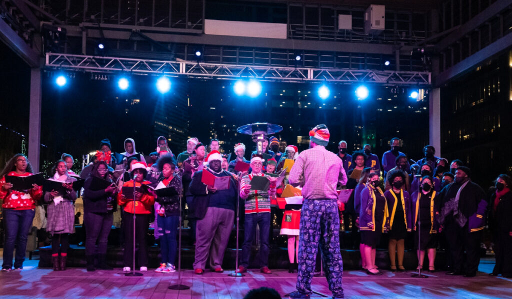 Carolers dressed in holiday clothing performing on a small stage