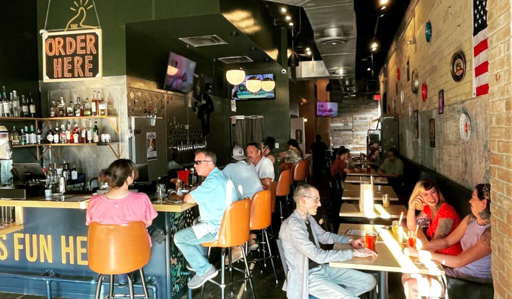 A narrow bar with people sitting in stools and at tables