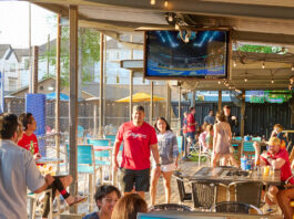 People walking through a covered patio area of a bar next to sand volleyball courts