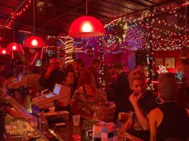 A bar scene decorated in red lights with people talking at the bar and in groups