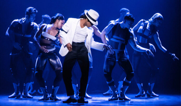 A performer in 'MJ' dancing, wearing a white hat and white jacket