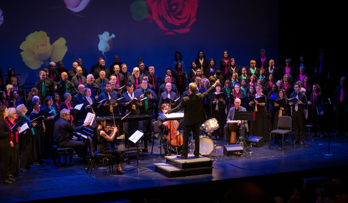 A chorus and band on stage performing with a conductor