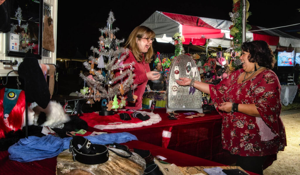 A vendor handing an object to a customer at a holiday-decorated booth