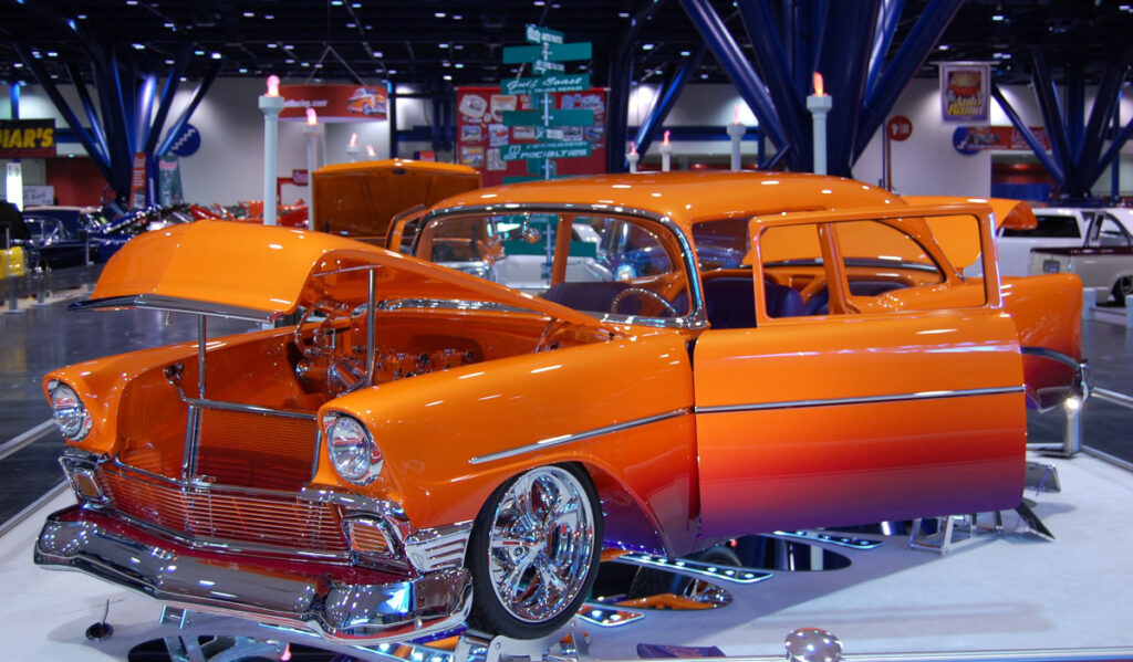 An orange and blue hot road with its hood and doors open on a platform