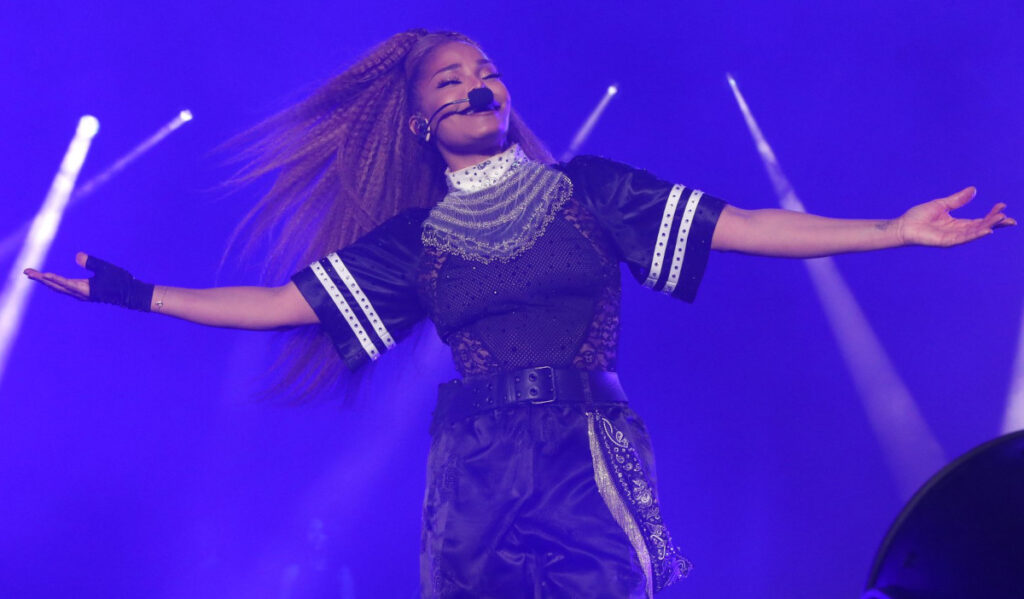 Janet Jackson performs on stage with her arms outstretched