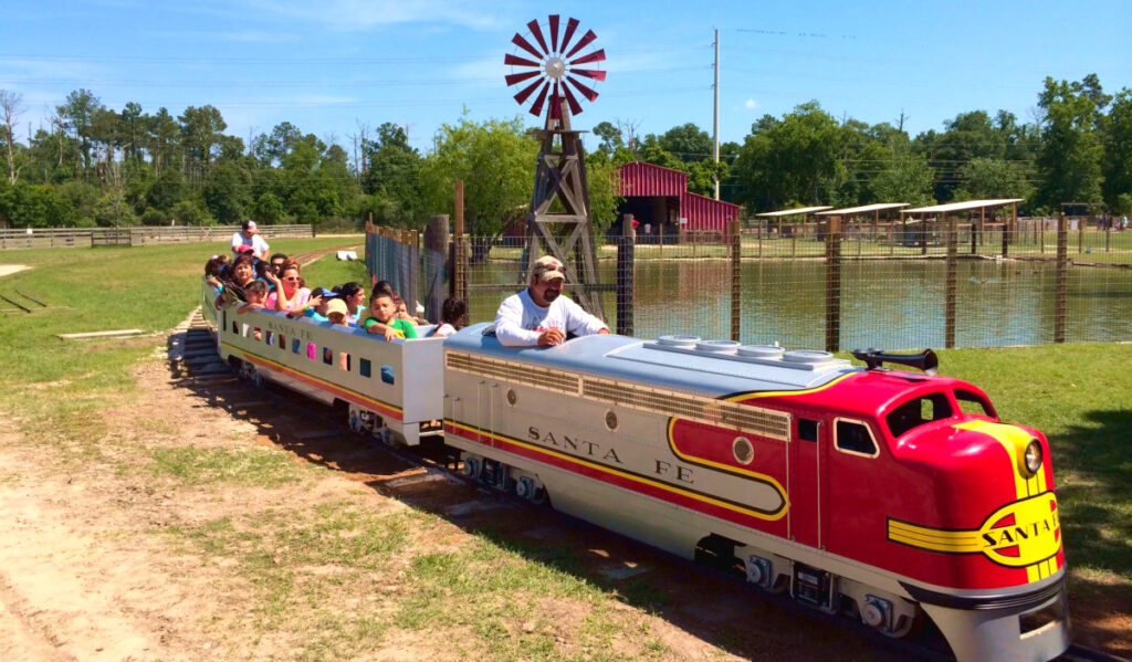 A miniature locomotive with children aboard passing by a body of water