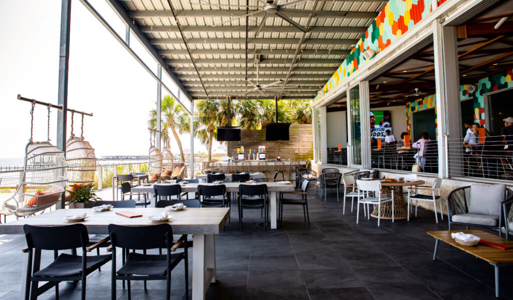 Exterior patio of Pier 6 with hanging chairs facing the water and empty tables and a bar