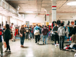 A marketplace filled with people walking around and t-shirts hanging in the background