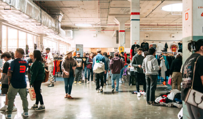 A marketplace filled with people walking around and t-shirts hanging in the background