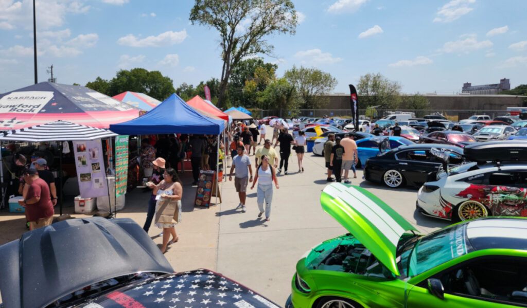 Crowds moving between market stalls and cars on display with their hoods open