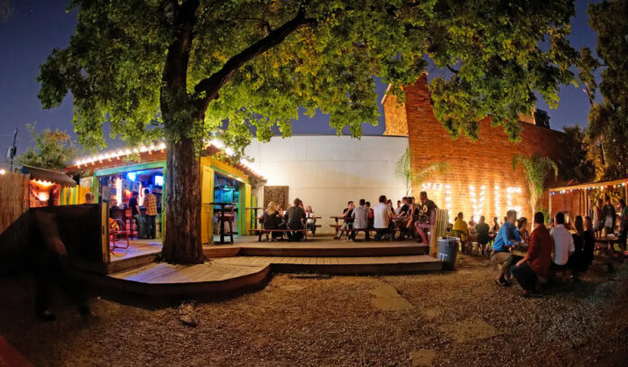 A backyard setting with people at tables and a light-up sign that says "Elvis"