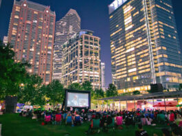 An outdoor movie screening at Discovery Green with towering skyscrapers behind the screen