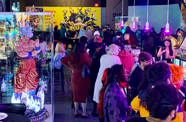 People crowded around a bar ordering drinks with anime statues and posters in the background
