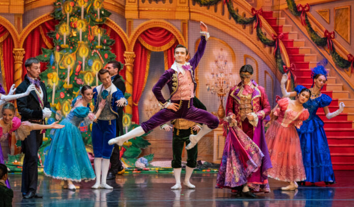 A ballet performer leaps as costumed performers look on during a Christmas scene