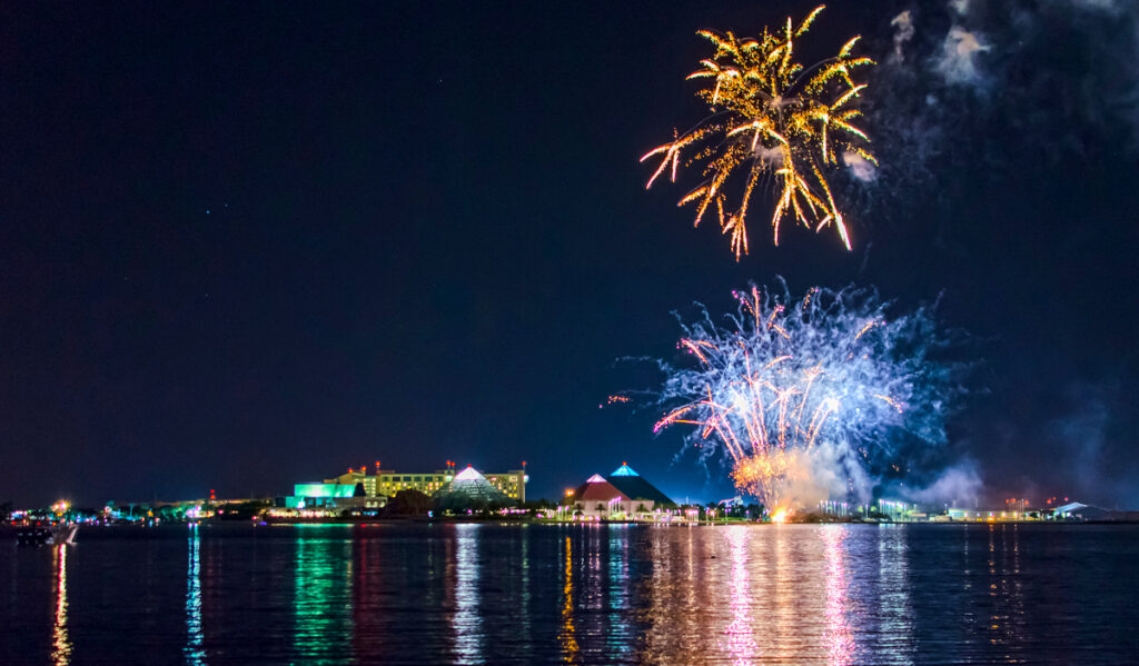 Fireworks exploding over a body of water near the Moody Gardens pyramids